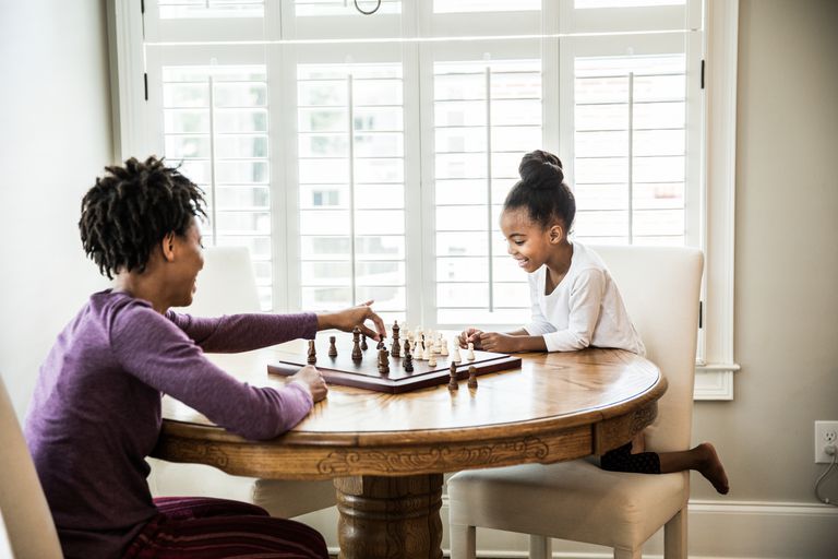 Млади girl (6yrs) playing chess with mother