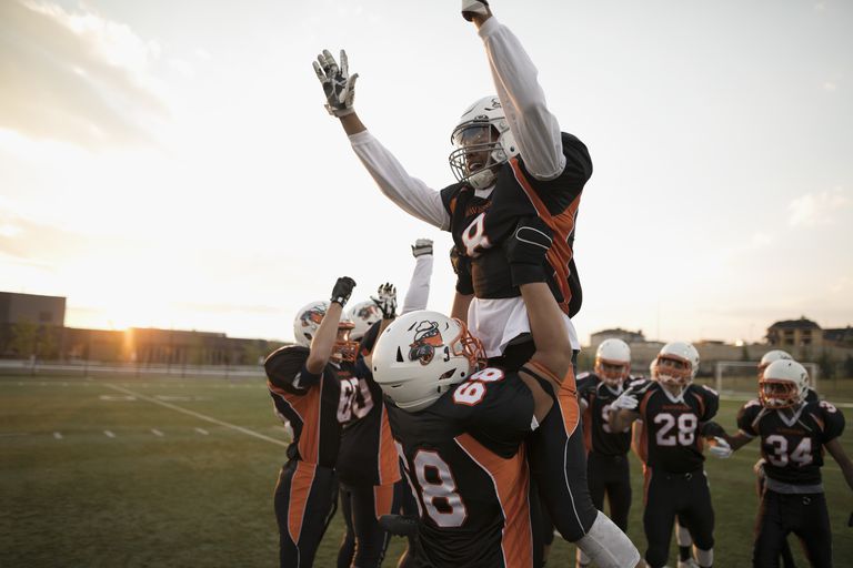 Теенаге boy high school football players lifting celebrating, cheering teammate on football field
