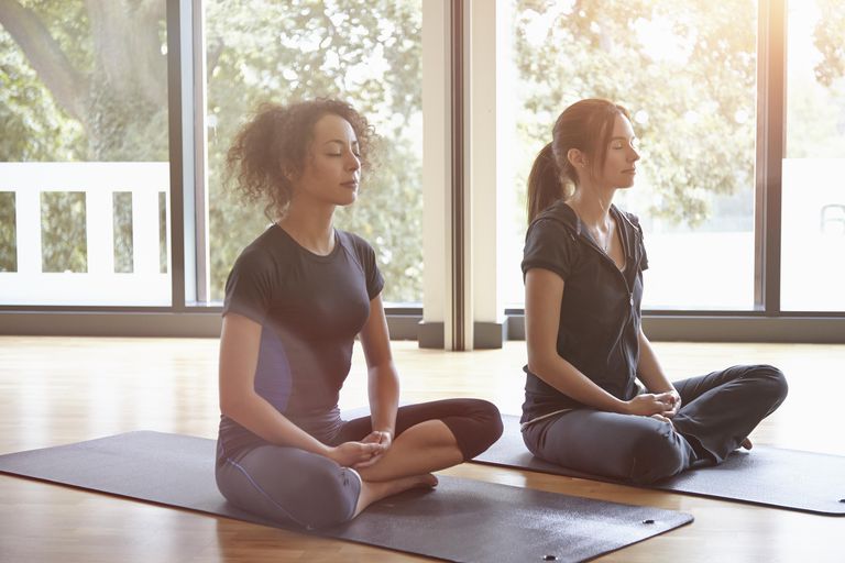 दो women sitting in a yoga class meditating