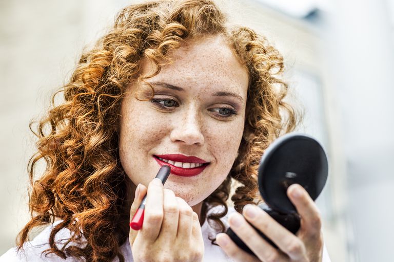 Portret of freckled young woman applying lipstick