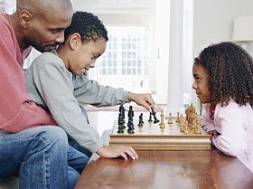 ए father plays chess with his kids.