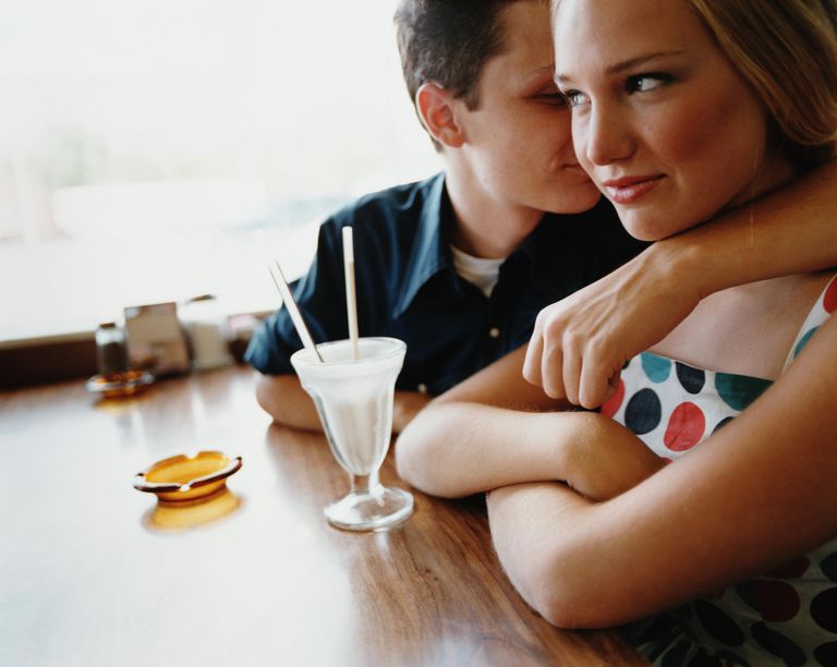 Млади romantic couple in diner, man's arm around woman