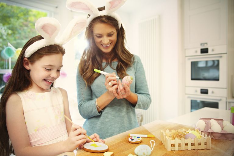 אִמָא and daughter wearing costume rabbit ears coloring Easter eggs and cookies