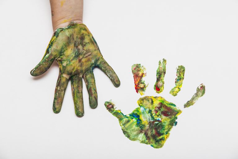 Otrok with colorful painted hand beside her hand print on paper