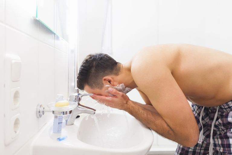 Genç man washing face in bathroom sink