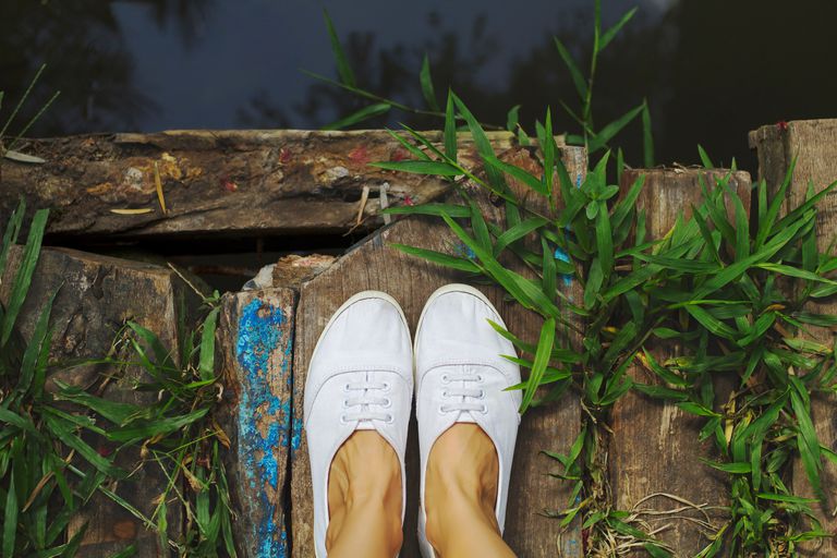 kvinna's feet in white sneakers standing on dock