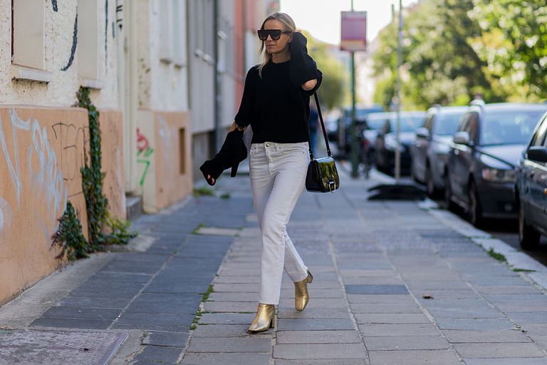 Žena wearing white jeans black sweater and gold ankle boots