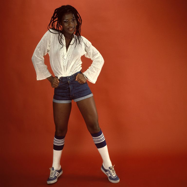 model wearing denim shorts, white shirt, and blue fashion sneakers. Photo taken in 1973.