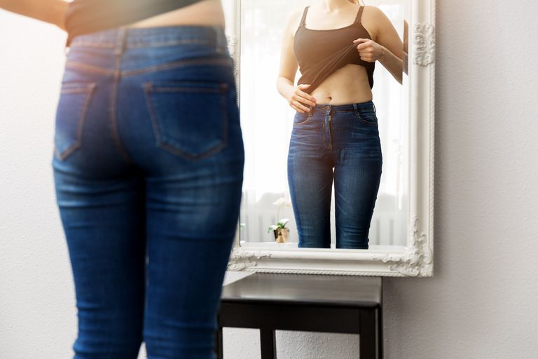 महिला in jeans looking in mirror at stomach