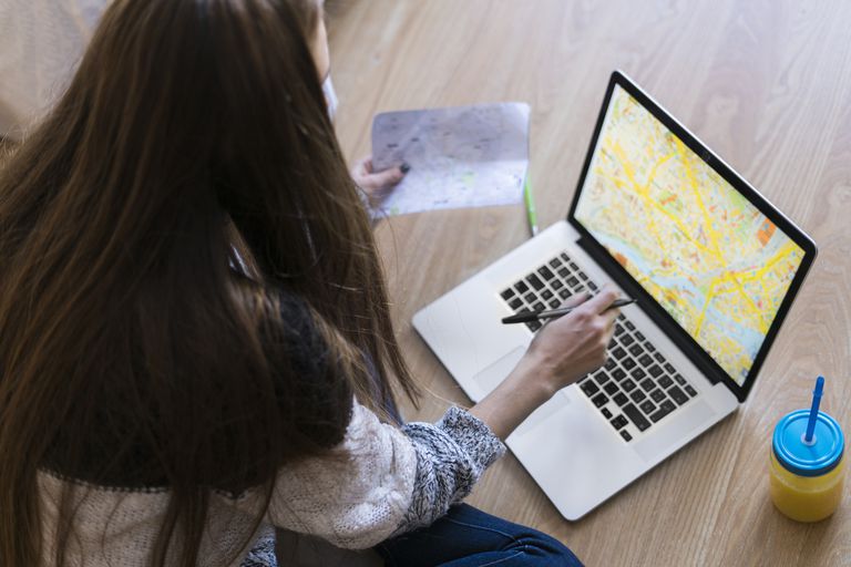 Ung woman sitting on the floor looking at map on laptop