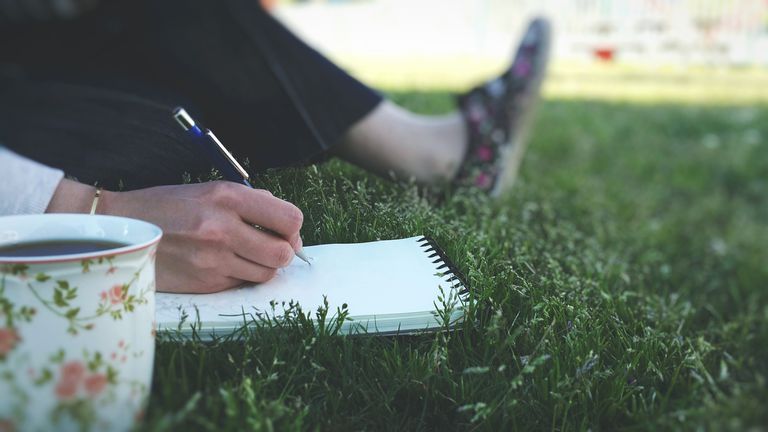 कम Section Of Woman Drawing While Sitting On Grassy Field