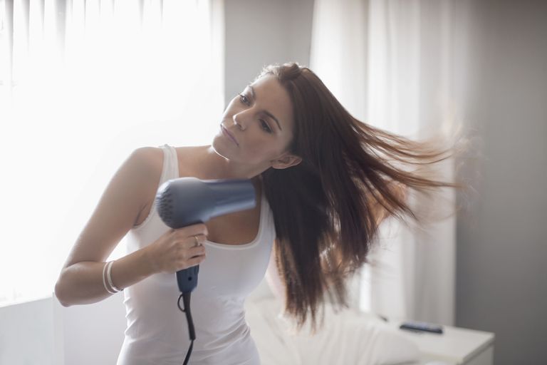 Млади woman holding hair-dryer, drying hair