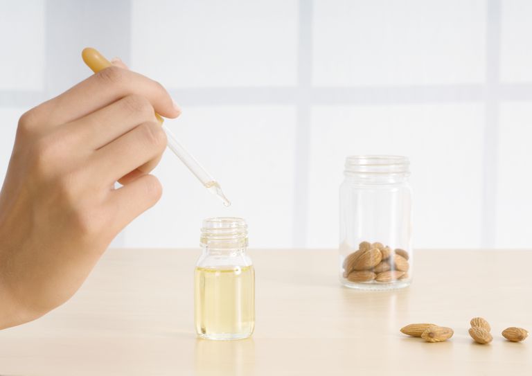 महिला's hand holding dropper of essential oil with almonds