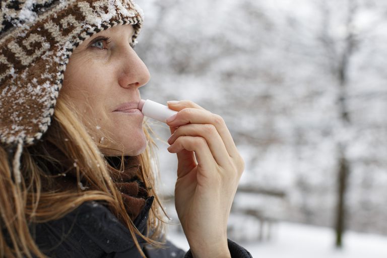 žena applying moisturizer to lips in winter