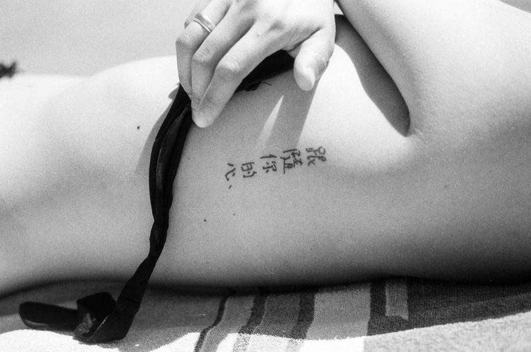 לְקַעֲקֵעַ in Chinese characters on a woman's ribs