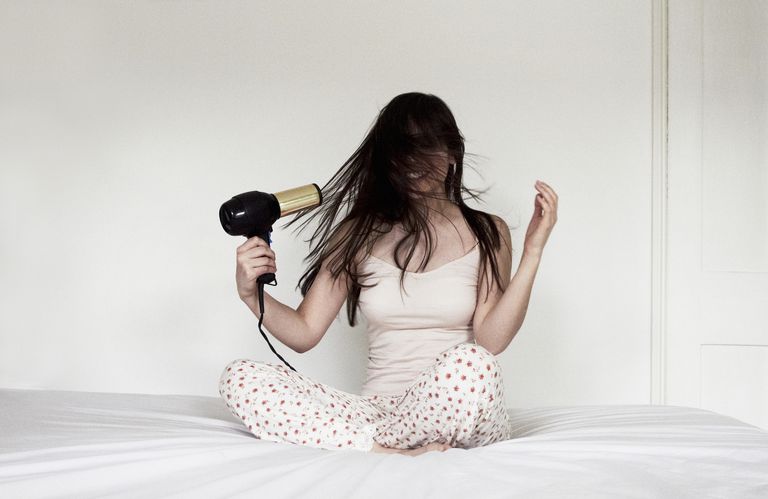 महिला sitting on bed blow drying hair
