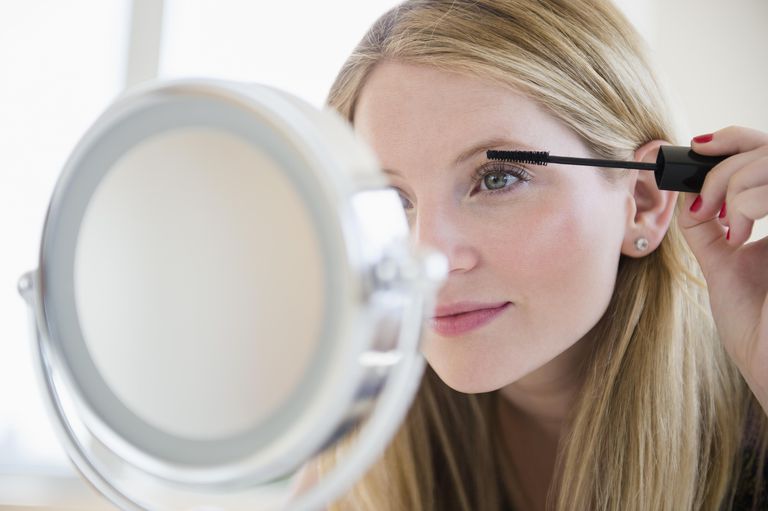 Жена putting on mascara in mirror